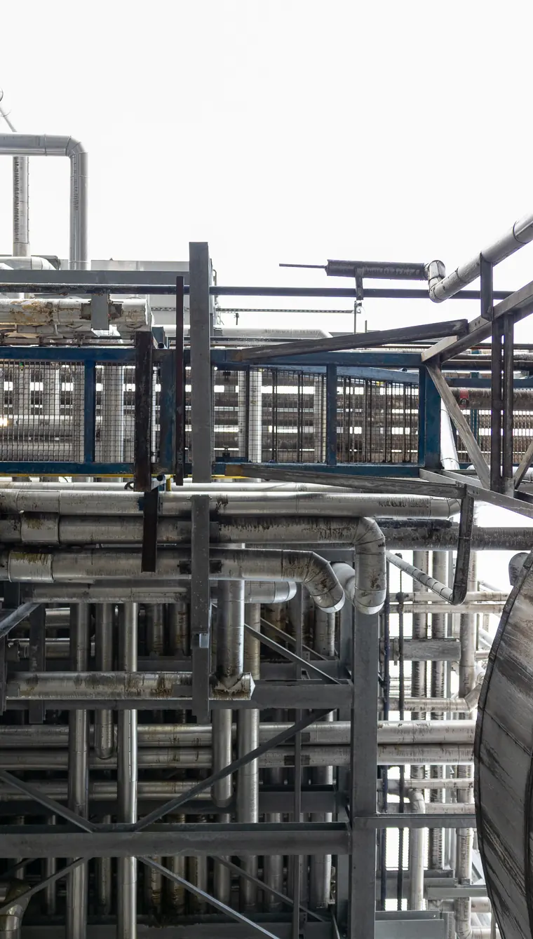 Close view of banked process pipework and steelwork on an outdoor rack, pipes running in parallel behind a blue guard rail.
